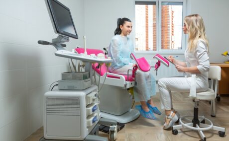 O femeie pe patul din cabinetul medicului ginecolog, care discută cu specialistul
