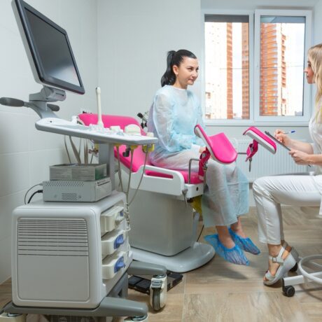 O femeie pe patul din cabinetul medicului ginecolog, care discută cu specialistul
