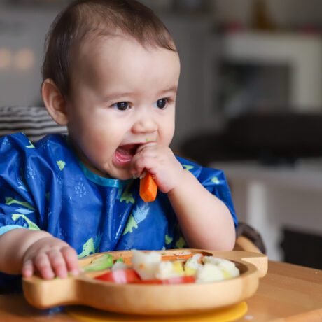 Un bebeluș autodiversificat, în scaunul de masă, în timp ce consumă alimente