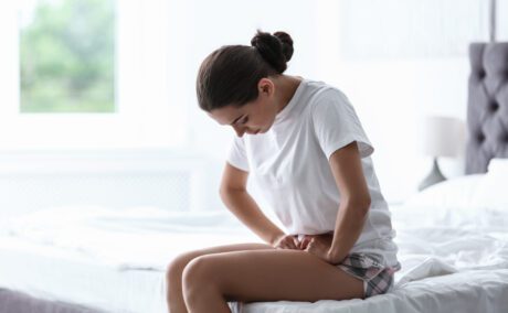 O femeie care stă pe marginea patului și se confruntă cu dureri date de endometrioză