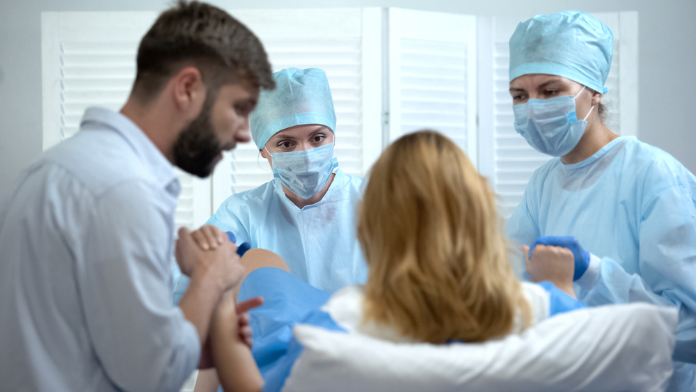 O femeie în sala de travaliu, pe masa de nașteri, cu medicii pe lângă ea