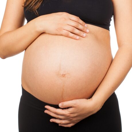 O femeie însărcinată, îmbrăcată cu top negru și colanți, cu burta descoperită, pe care are o linie verticală, numită linea nigra