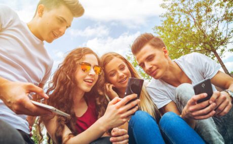 Patru adolescenți care se uită pe telefon, fotografiați în timpul unei ieșiri în aer liber