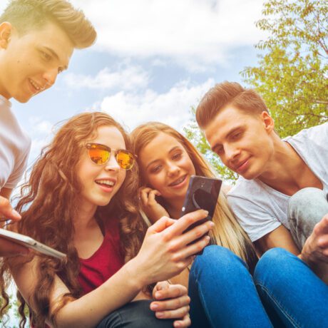 Patru adolescenți care se uită pe telefon, fotografiați în timpul unei ieșiri în aer liber