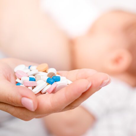O femeie care ține în mână mai multe pastile și are un bebeluș la sân