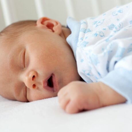 Bebeluș care doarme cu gura deschisă, în pătuț și are un body bleu cu alb, ilustrând rutina de somn a bebelușului