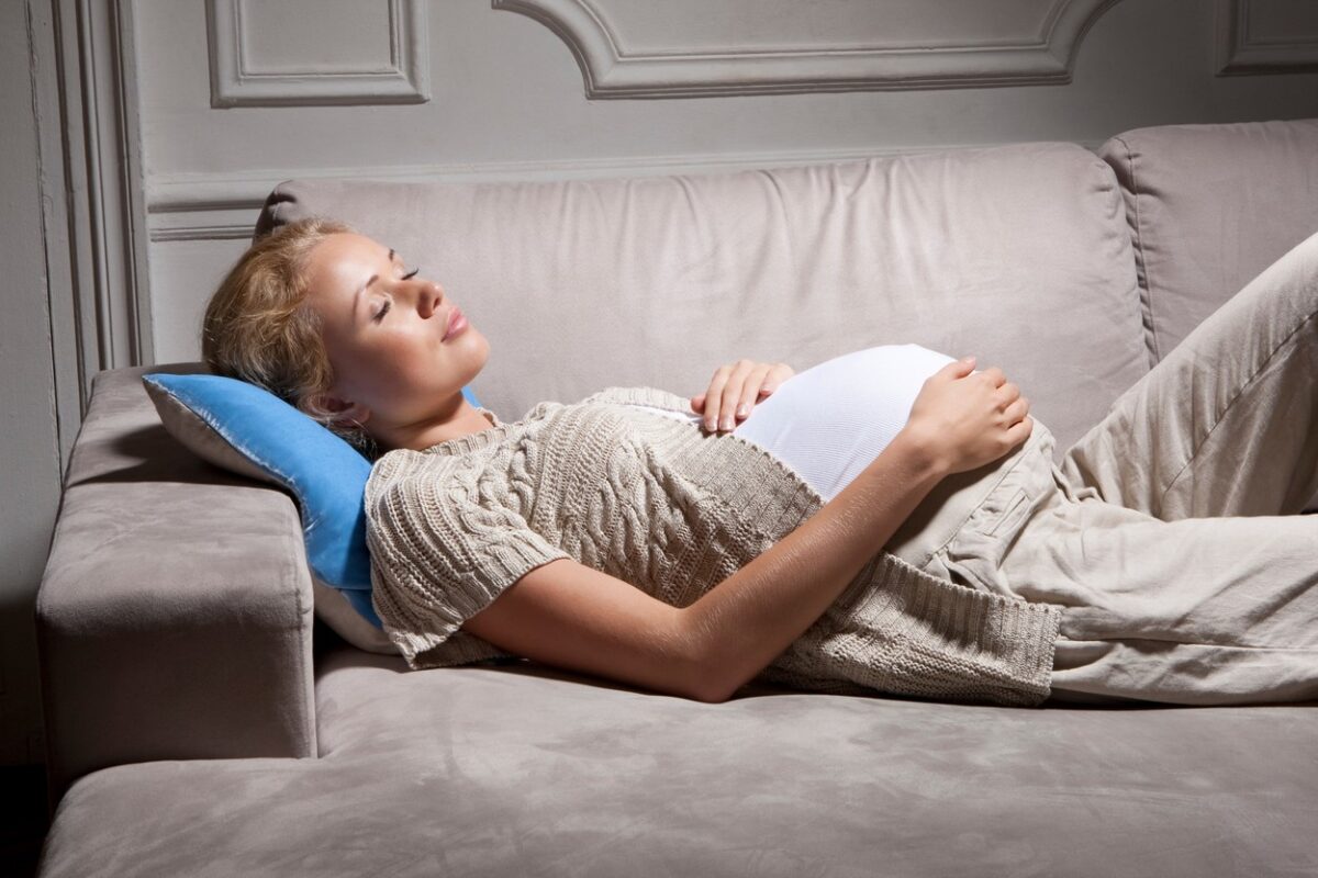 O femeie însărcinată care doarme pe o canapea, cu o pernă sub cap și cu mâna pe burtă