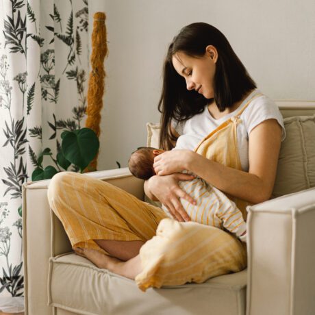 O mamă care își alăptează bebelușul în intimitatea casei, pe un fotoliu