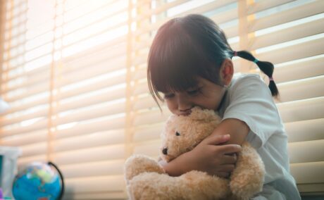 O fetiță care stă cu ursulețul de pluș în brațe, supărată