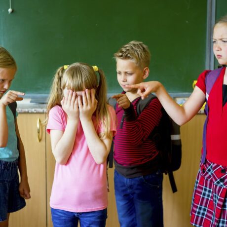 Copii la școală, care agresează o fetiță, arătând-o cu degetul și ea își acoperă fața cu mâinile