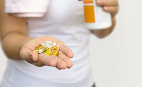 O femeie în tricou alb, cu mai multe feluri de vitamine prenatale în mână
