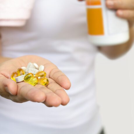 O femeie în tricou alb, cu mai multe feluri de vitamine prenatale în mână
