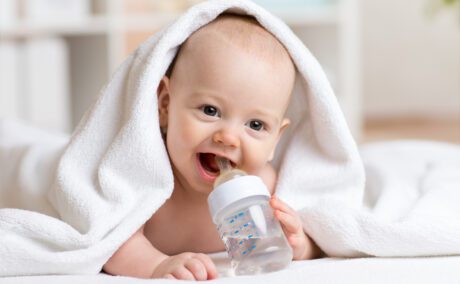 Un bebeluș care bea apă dintr-un biberon, acoperit de un prosop de baie