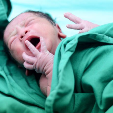 Un bebeluș care plânge, imediat după naștere, înfășurat într-o păturică verde