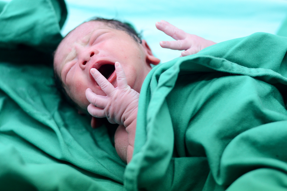 Un bebeluș care plânge, imediat după naștere, înfășurat într-o păturică verde