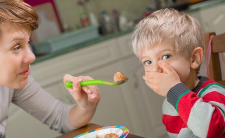 Mama care stă cu copilul la masă, în bucătărie, și îi oferă copilului mâncare într-o linguriță verde, iar acesta o refuză, punând mâna la gură, ilustrând de ce sunt copiii mofturoși la masă