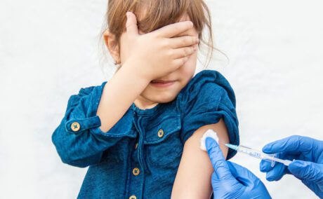 O fetiță care pune mâna la ochi atunci când primește vaccinul antigripal