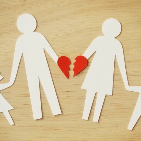O familie cu doi copii, realizată din hârtie albă, decupată, iar părinții sunt despărțiți de o inimă roșie, care ilustrează cum să le spui copiilor despre divorț