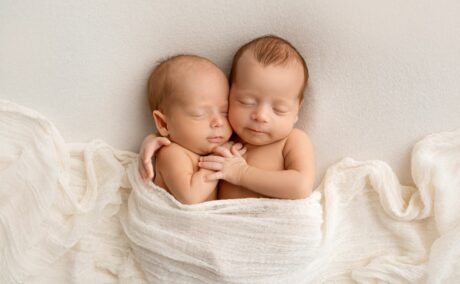 Bebeluși, gemeni, care se stau îmbrățișați și unt acoperiți cu o eșarfă albă