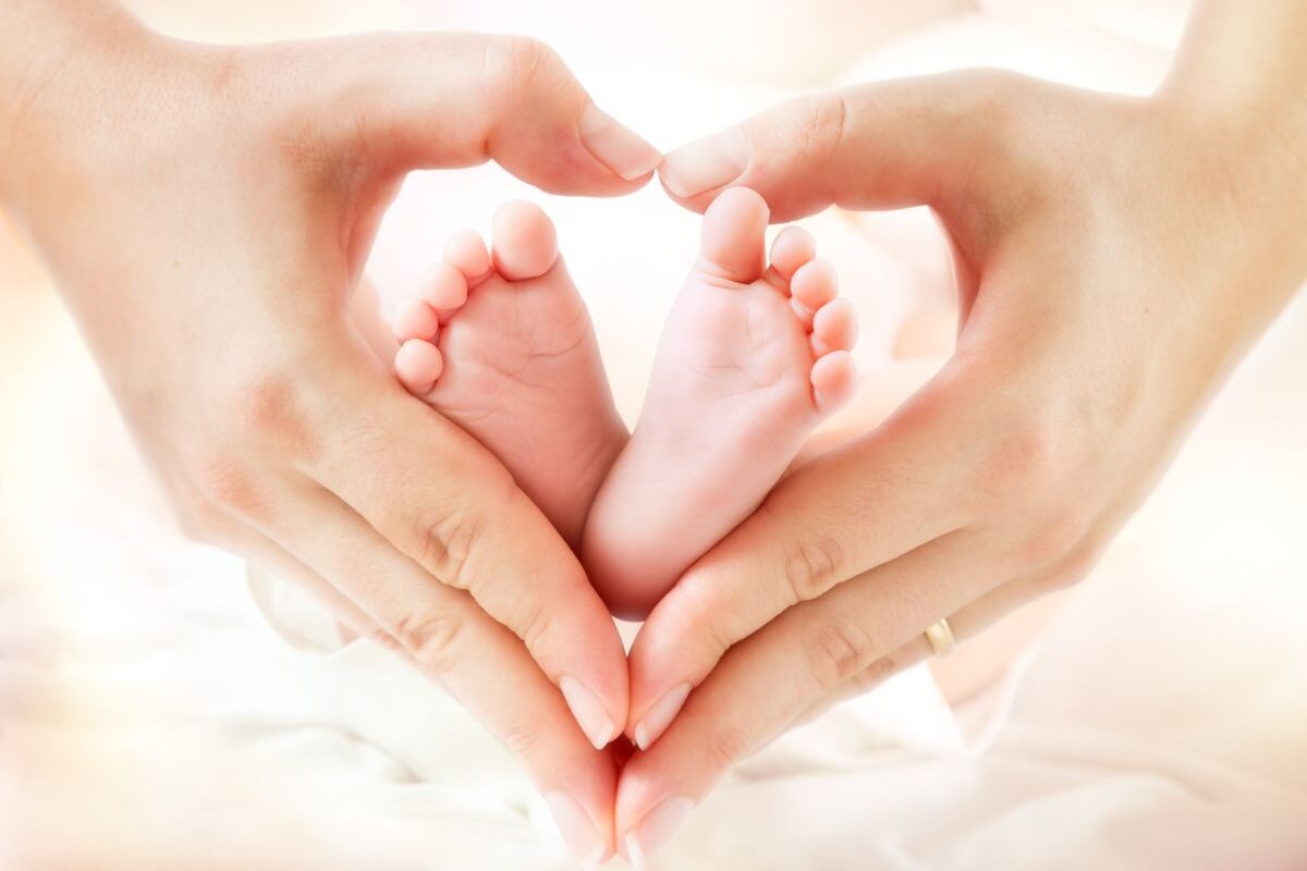 Mâini ținute în formă de inimioară, care țin două tălpi de bebeluș