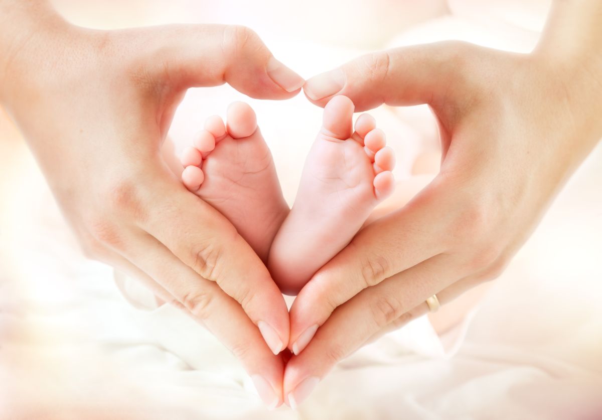 Mâini ținute în formă de inimioară, care țin două tălpi de bebeluș