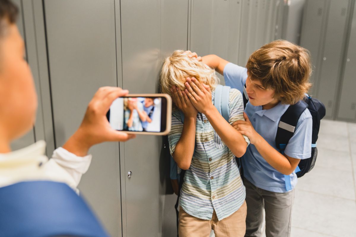 Bullying cibernetic, în care un copil filmează în timp ce un copil îl agresează pe altul prinzândul din spate de o mână și de gât, iar celălat se apără ținând mainile la față