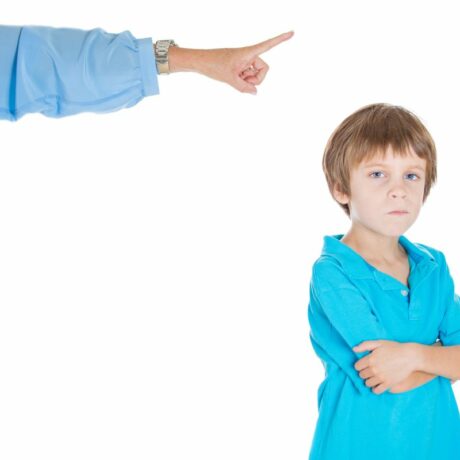 Mâna unei mame, îmbrăcae cu o cămașă albastră, care arată cu degetul spre un copil îmbrăcat cu un tricou albastru, care stă cu mâinile încrucișate, ilustrând comportamentul sfidător la copii