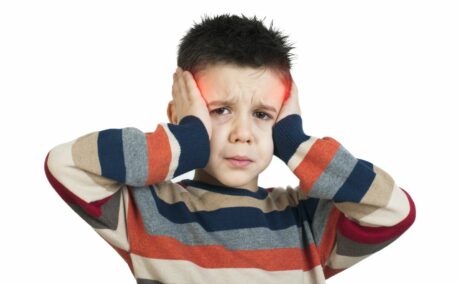 Băiat, îmbrăcat cu un pulover cu dungi colorate, se ține cu mâinile de tâmple și zona este înroșită pentru a sugera durerile de cap la copii