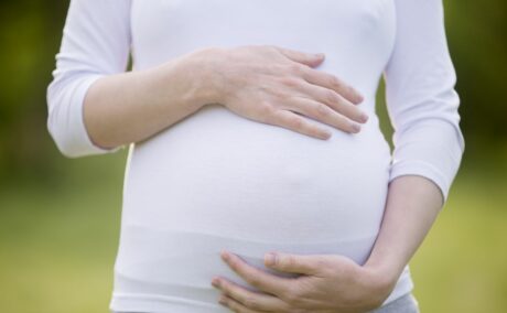 Femeie însărcinată, în parc, îmbrăcată cu o bluză albă și colanți gri, care se ține cu mâinile de burtă, ilustrând pierderea sarcinii în trimestrul 2