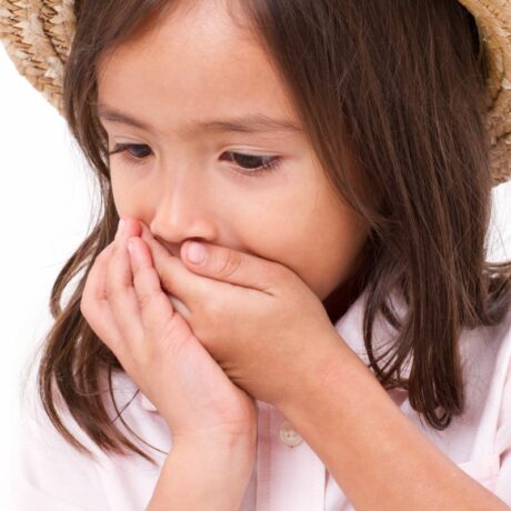 Fetiță, care are o pălărie din paie pe cap, și o bluză albă cu mâneci scurte, cu nasturi albi, care se ține cu mâinile de gură pentru a ilustra frica de vomă la copii