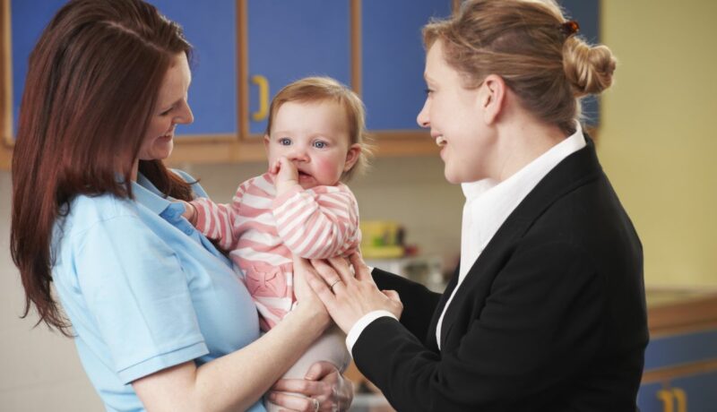 Un bebeluș care este ținut în brațe de mamă și care interacționează cu o altă femeie