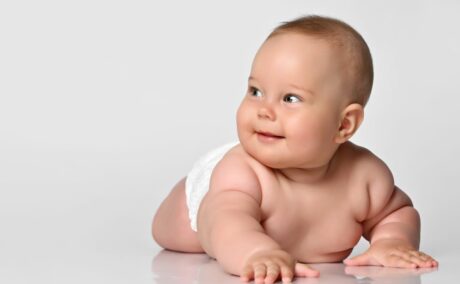 Bebeluș cu macrosomia fetală, care are scutec și este așezat pe burtă și se sprijină pe brațe, ținându-și capul ridicat
