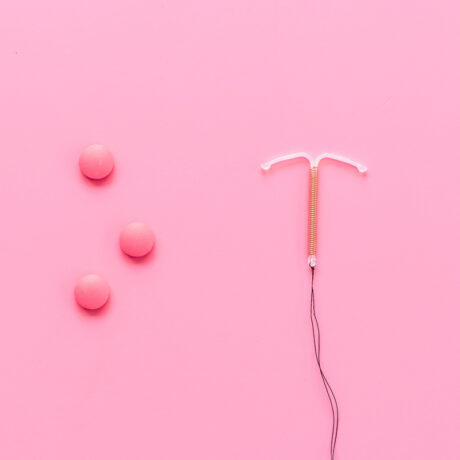 Pastile roz contraceptive și un sterilet, pe un fundal roz, utilizate pentru a ilustra contracepția potrivită în timpul alăptării