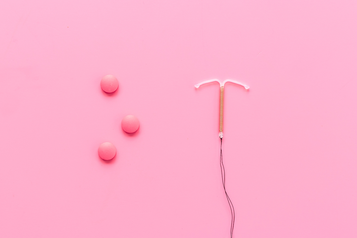Pastile roz contraceptive și un sterilet, pe un fundal roz, utilizate pentru a ilustra contracepția potrivită în timpul alăptării