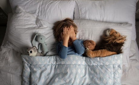 O fotografie cu un băiețel așezat în pat, alături de animale de pluș, folosită pentru a ilustra coșmarurile la copii