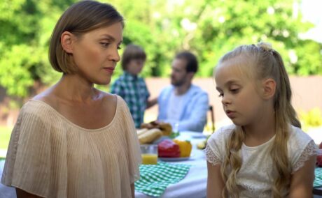 Mama, îmbrăcată cu o bluză bej care se uită spre fiica ei și stau cu spatele la o masă câmpenească, organizată în curte, und emai sunt și alți membrii ai familiei, iar pe fundal se vede și o pădure înverzită, ilustrând faptul că îți faci copilul de rușine