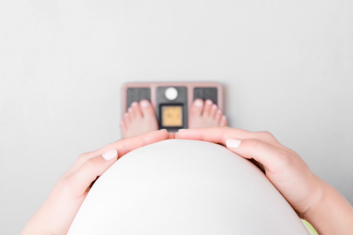 O femeie însărcinată, așezată pe un cântar pentru a măsura greutatea ideală în sarcină