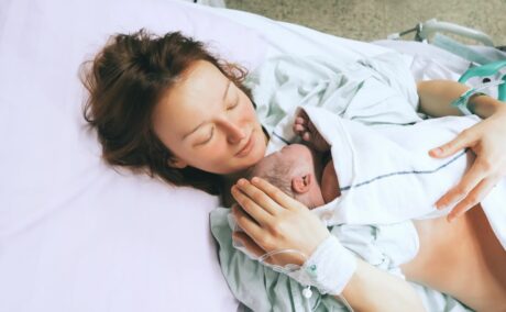Femeie, care abia a născut, se bucură de de ora magică alături de bebelușul ei, pe care îl ține pe piept, în timp ce stă întinsă pe pat