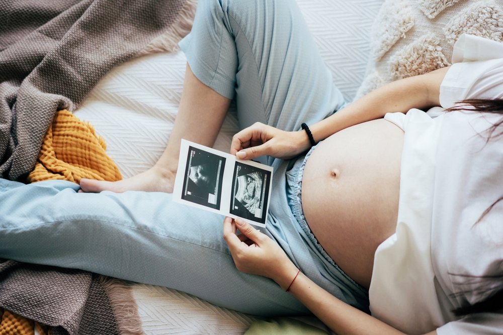 O femeie însărcinată în trimestrul trei, cu ecografia bebelușului în mâini