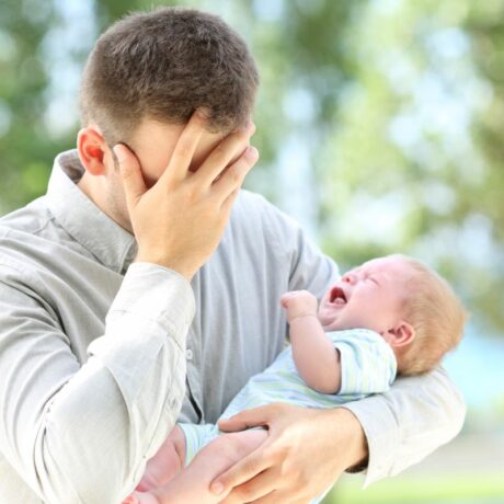 Tată ieșit în parc cu bebelușul, care își ține mâna pe față, ilustrând 10 probleme în căsnicie care apar după nașterea celui de-al doilea copil 