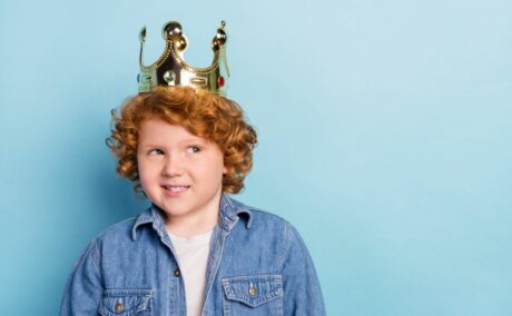Băiețel roșcat, cu tricou alb și jachetă din denim, pe un fundal bleu, care are pe cap o coroană de rege, ilustrând 3 greșeli de parenting care îi fac pe copii narcisiști