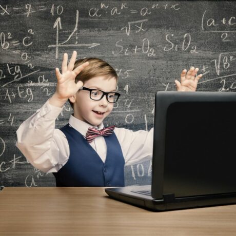 Băiețel cu ochelari de vedere, îmbrăcat cu cămașă albă, vestă bleumarin și papion cu dungi roșii, care stă la birou, cu mâinile ridicate, având în față un laptop, iar în spate are o tablă pe care sunt scrise formule matematice, ilustrând 5 probleme pe care le pot avea copiii supradotați