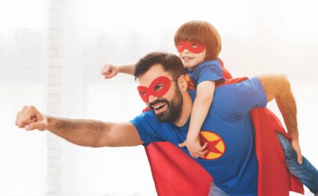 Tată și fiu, îmbrăcați în costume de super-eroi, albastre cu roșu și ochelari roșii, tatăl având pe piept o stea roșie într-un cerc galben, iar băiețelul stă în spatele tatălui, ilustrând ce înseamnă să fii un tată bun