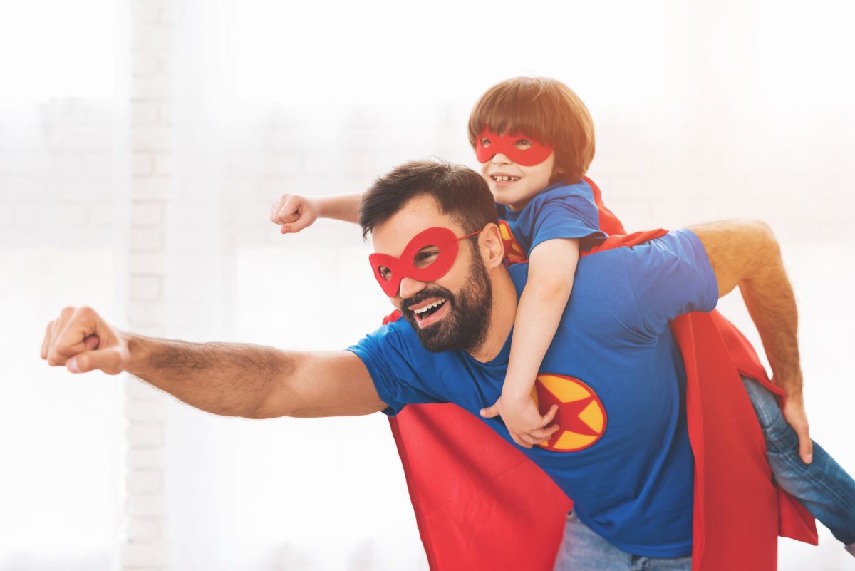 Tată și fiu, îmbrăcați în costume de super-eroi, albastre cu roșu și ochelari roșii, tatăl având pe piept o stea roșie într-un cerc galben, iar băiețelul stă în spatele tatălui, ilustrând ce înseamnă să fii un tată bun
