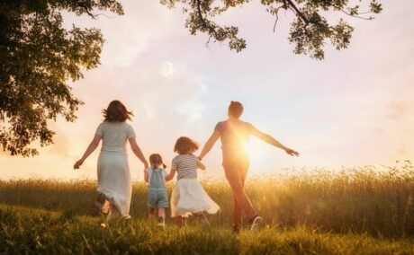 Familie cu două fetițe, care aleargă pe un cîmp, stând cu spatele, lângă o pădure, la apus de soare, ilustrând parentingul anti-dopamină
