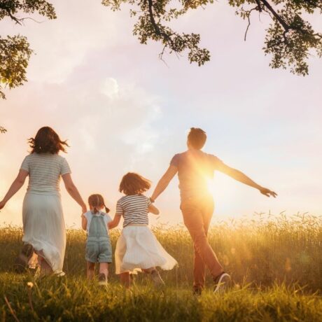 Familie cu două fetițe, care aleargă pe un cîmp, stând cu spatele, lângă o pădure, la apus de soare, ilustrând parentingul anti-dopamină