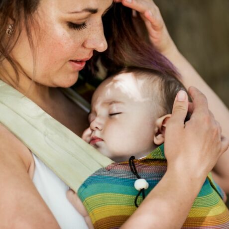 Mămică, îmbrăcată cu un maiou alb, care ține un bebeluș într-un sistem de purtare, ilustrând purtarea bebelușului