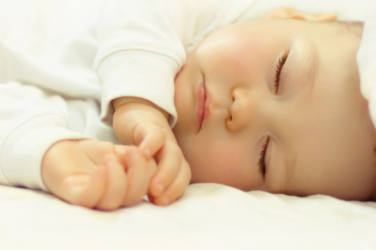 Bebeluș, îmbrăcat într-un body alb, care doarme pe-o parte, ilustrând regresia de somn la bebeluși
