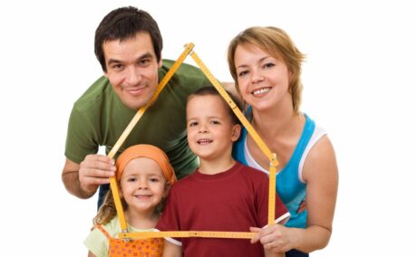 Familie formată din mamă, tată, băiat școlar și fată preșcolar, mama și tatăl țin în față un centimetru din lemn în formă de casă, ilustrând sfaturi pentru crearea listei cu regulile familiei