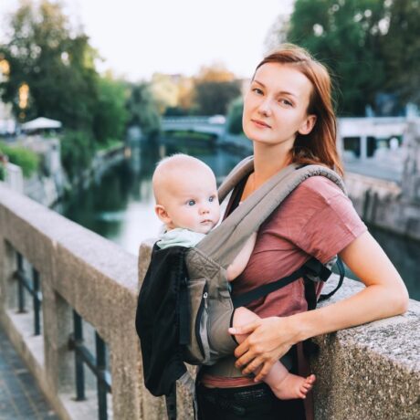 Mămică cu părul șaten, cu bebelușul în marsupiu, pe un pod